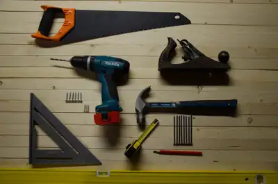 Assorted hand tools laid out deliberately on a wooden surface, including a saw, drill, plane, and tape measure