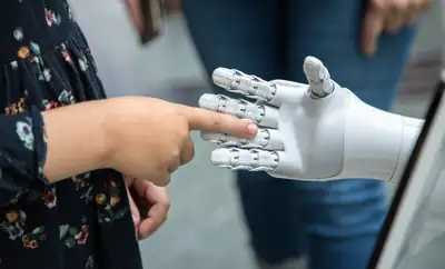 A person holding a robotic hand, representing the intersection of technology and humanity